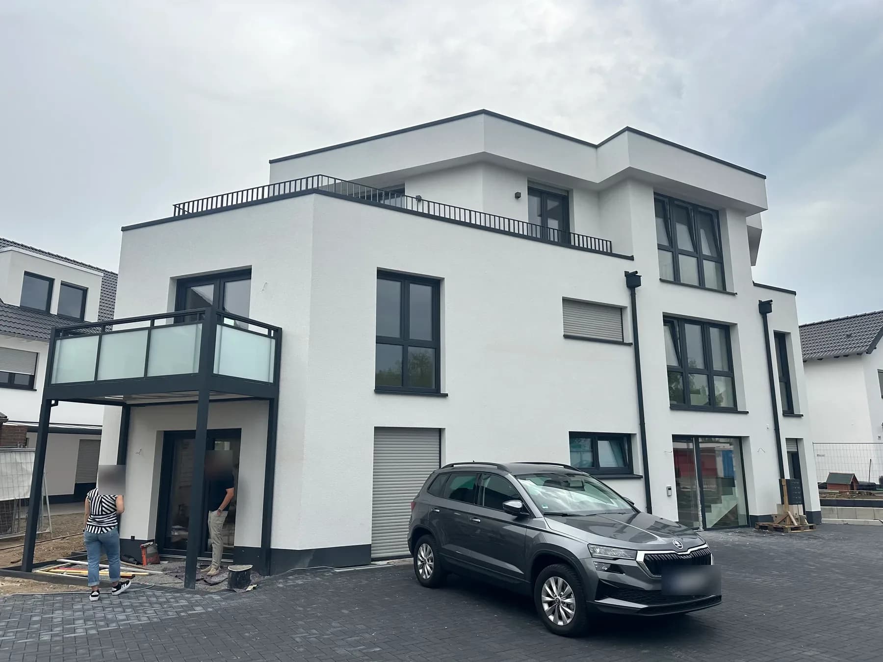 Fertiggestelltes Fünffamilienhaus mit weißem Putz, dunklen Fenstern und Balkon über dem Eingang