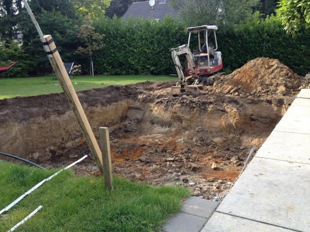 Baugrube für den Pool mit Minibagger und Aushub im Garten