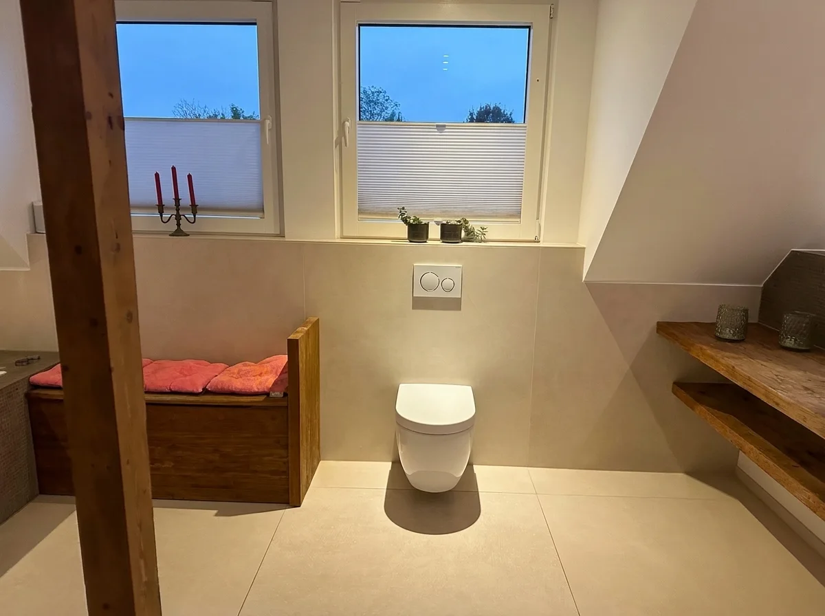 Wand-WC vor deckenhoch gefliester Wand, daneben Sitztruhe und offenes Holzbord