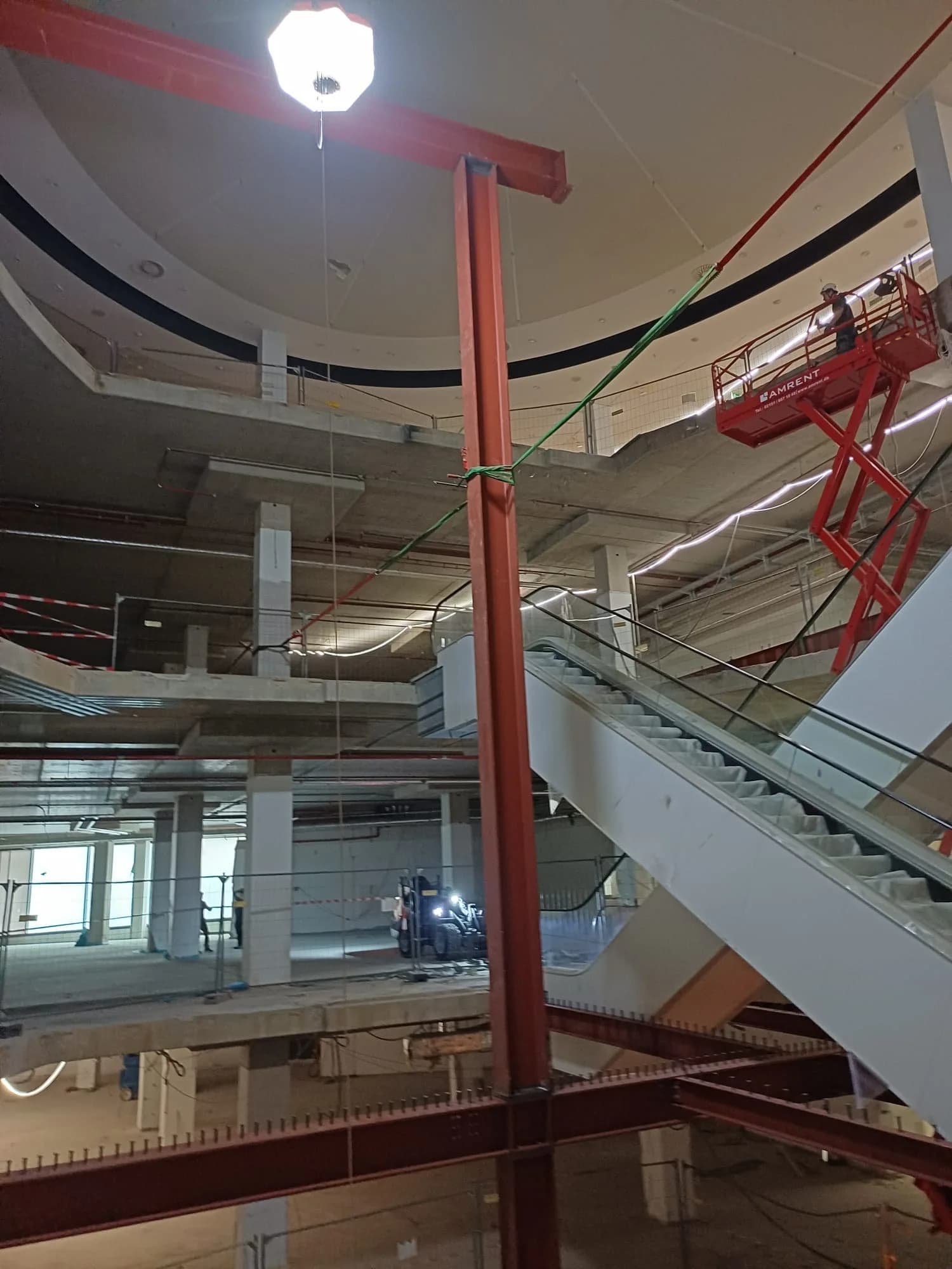 Umbau im Einkaufszentrum: rot grundierte Stahlstütze, dahinter eine gesetzte Rolltreppe und die runde Deckenöffnung