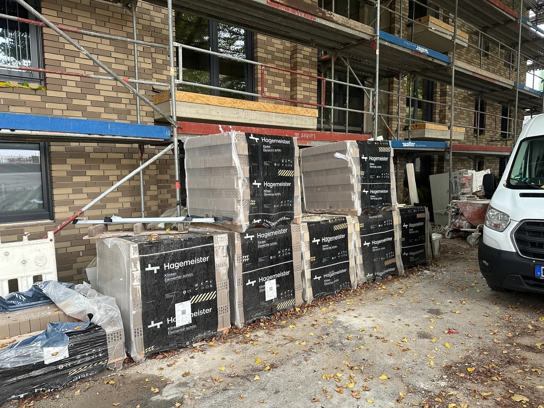 Baustelle mit Gerüst und Paletten Verblendklinker vor dem halbfertigen Mauerwerk