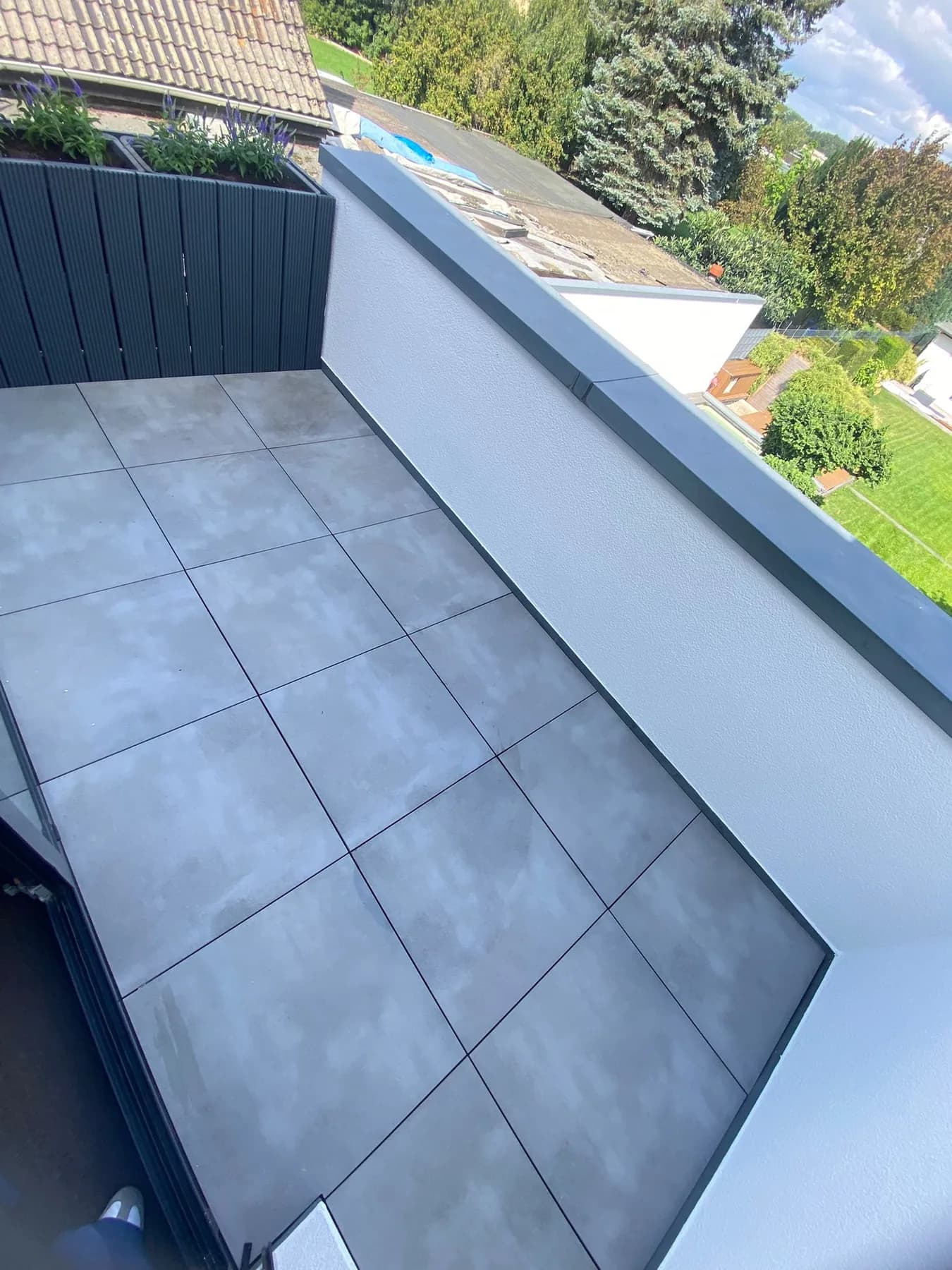 Balkon mit grauen Keramikplatten, Sichtschutz aus dunklen Lamellen und Blick über die Nachbardächer