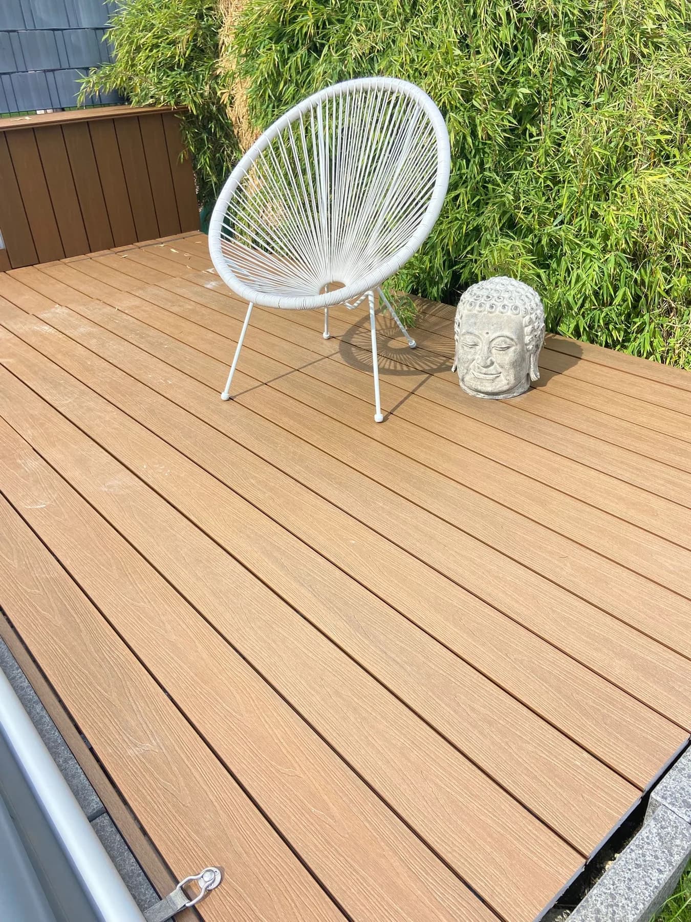 WPC-Terrassendiele in Teak am Pool, weißer Sessel vor einer Bambushecke