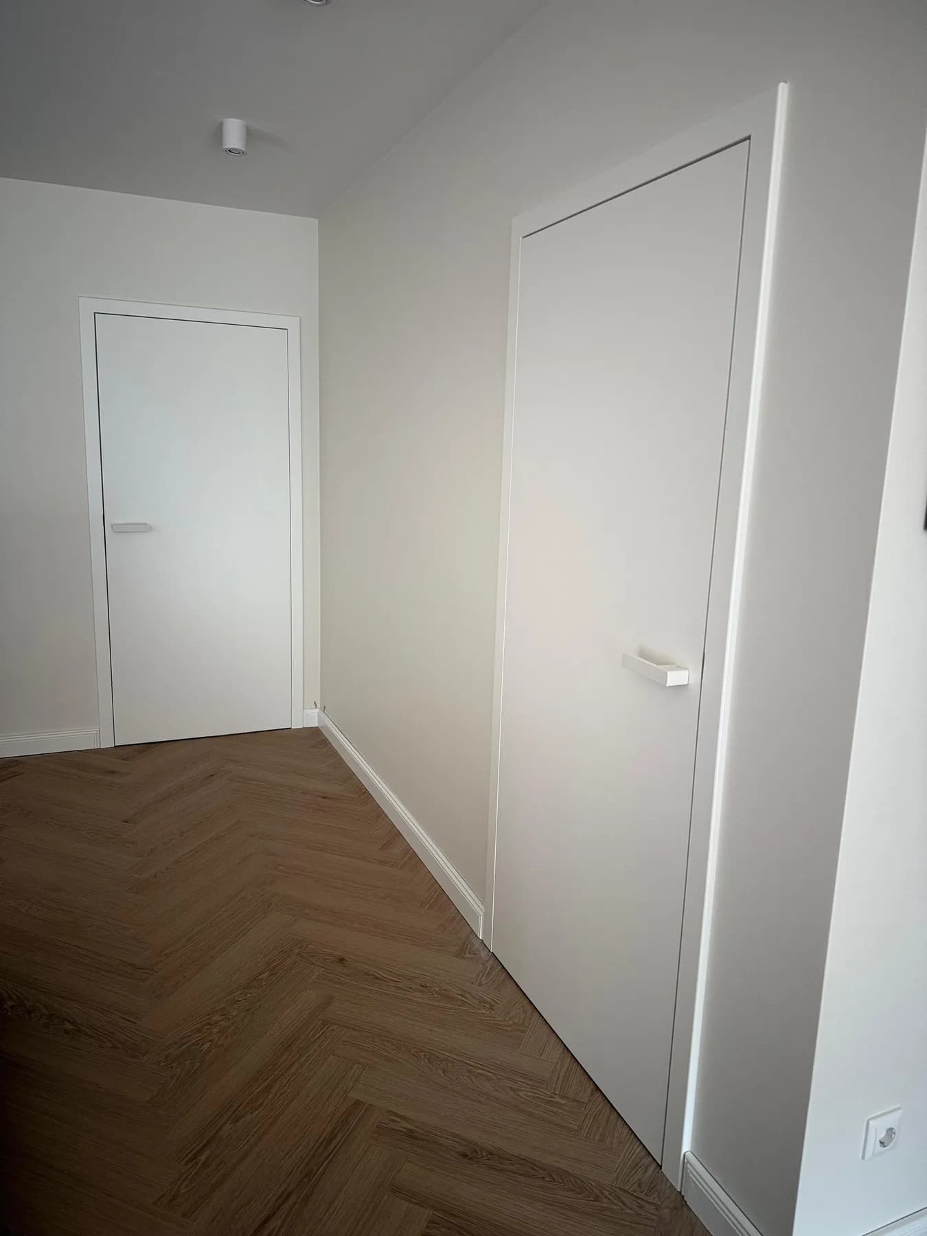 Flur mit zwei flächenbündigen weißen Türen und Fischgrätparkett